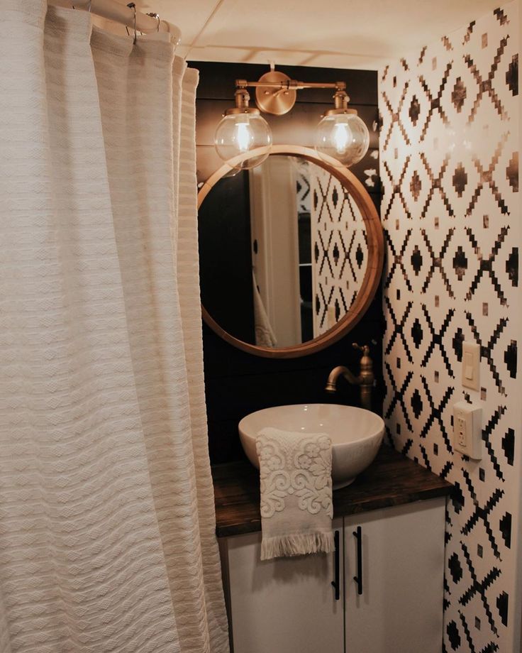 a white sink sitting under a bathroom mirror next to a shower curtain with lights on it