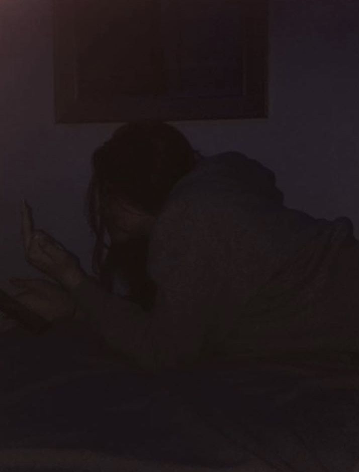 a woman laying in bed looking at her cell phone with the light shining on her