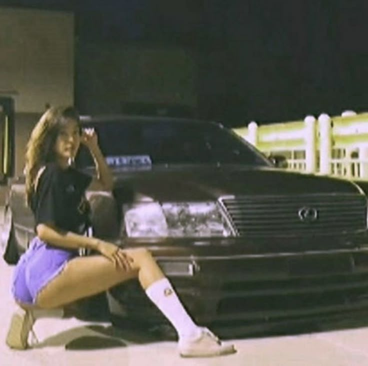 a woman sitting on the ground next to a parked car in front of a building