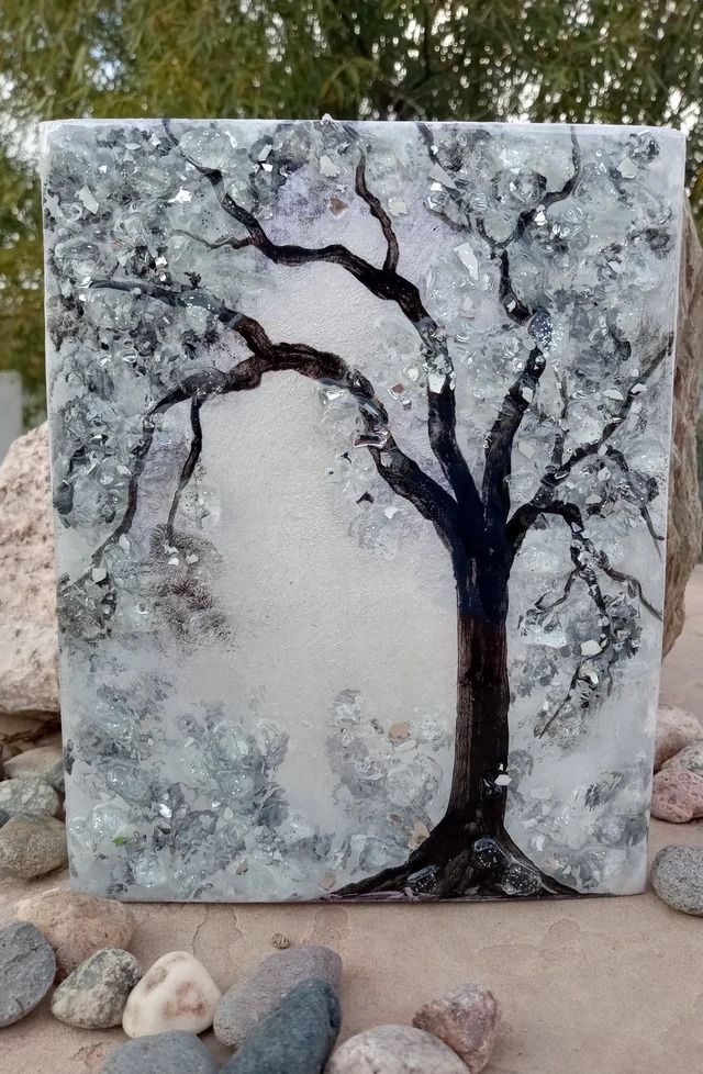 a glass block with a tree painted on it and rocks in the foreground next to it