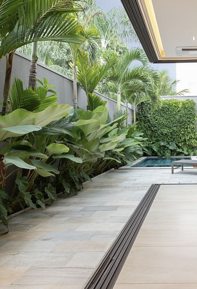 an outdoor swimming pool surrounded by greenery and palm trees, with a bench in the foreground