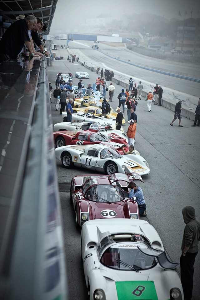 a row of race cars lined up on the track with people standing around looking at them