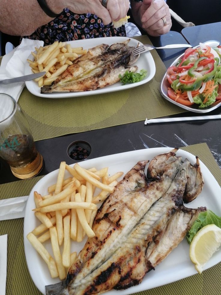 two plates with fish, fries and salad are on the table next to each other