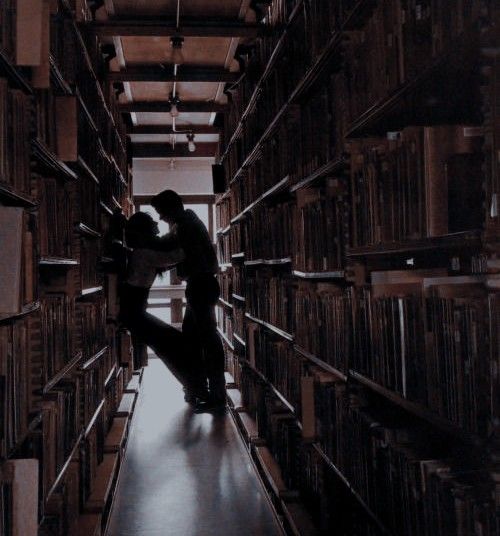 two people are kissing in the middle of a library full of record cases and books