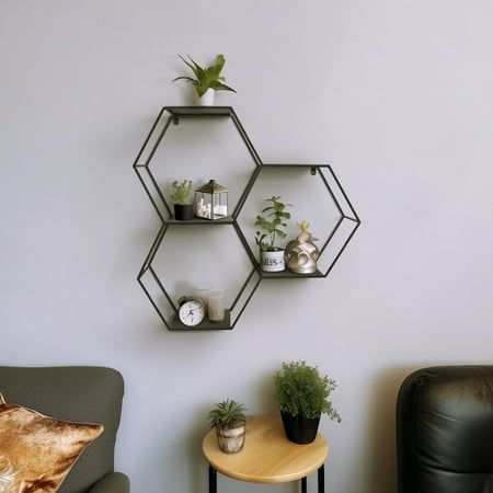 three hexagonal shelves on the wall above a table with two potted plants