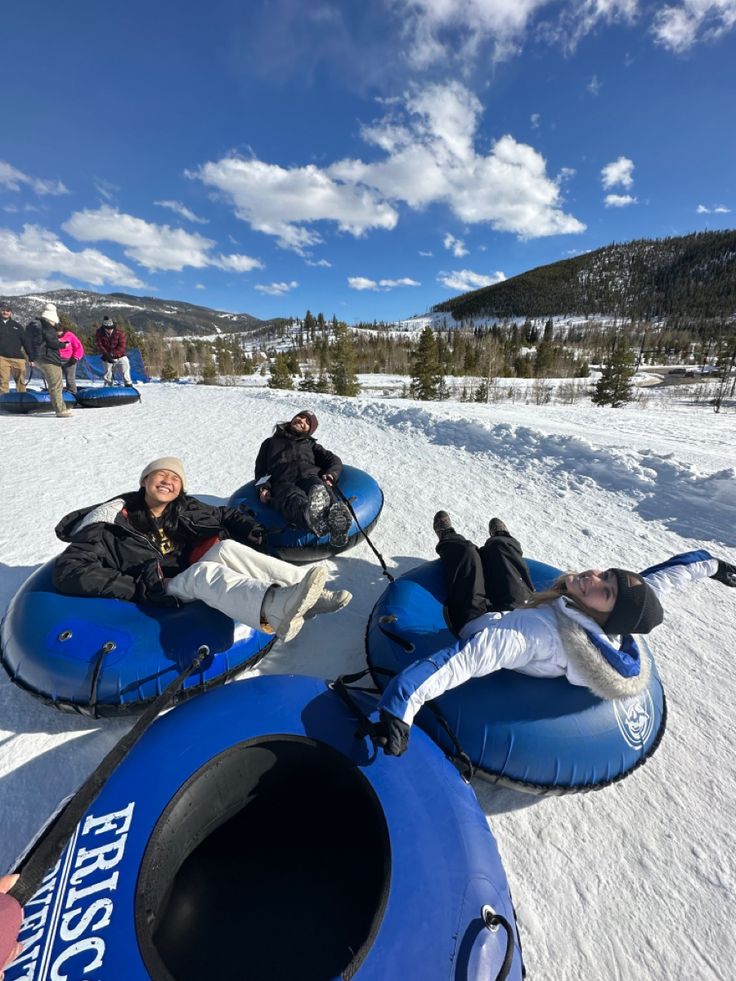 three people sitting on snow tubes in the snow