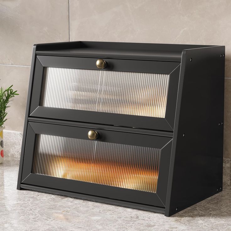 a black cabinet with two drawers on top of it next to a potted plant