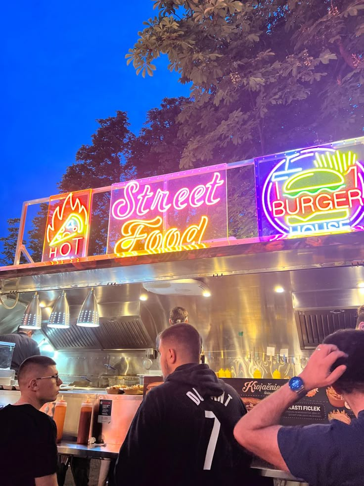 people standing in line to order food at a fast food restaurant with neon signs above them