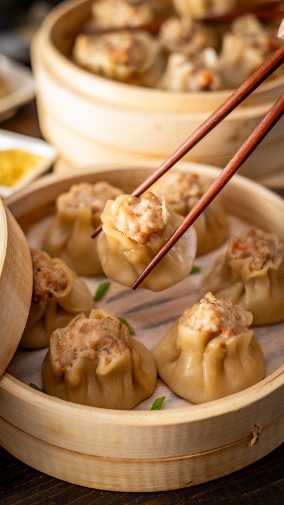 chopsticks picking up some dumplings in a wooden container with other food items