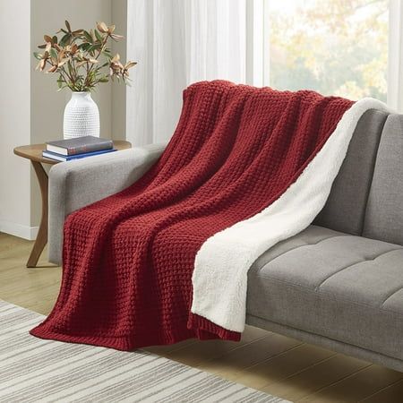 a couch with a red blanket on top of it next to a white rug and window