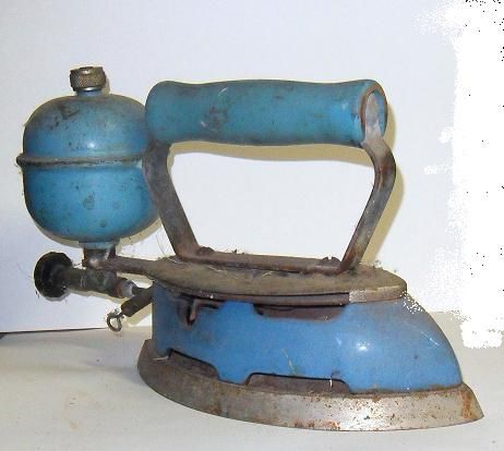 an old blue and silver iron sitting on top of a white table next to a wall