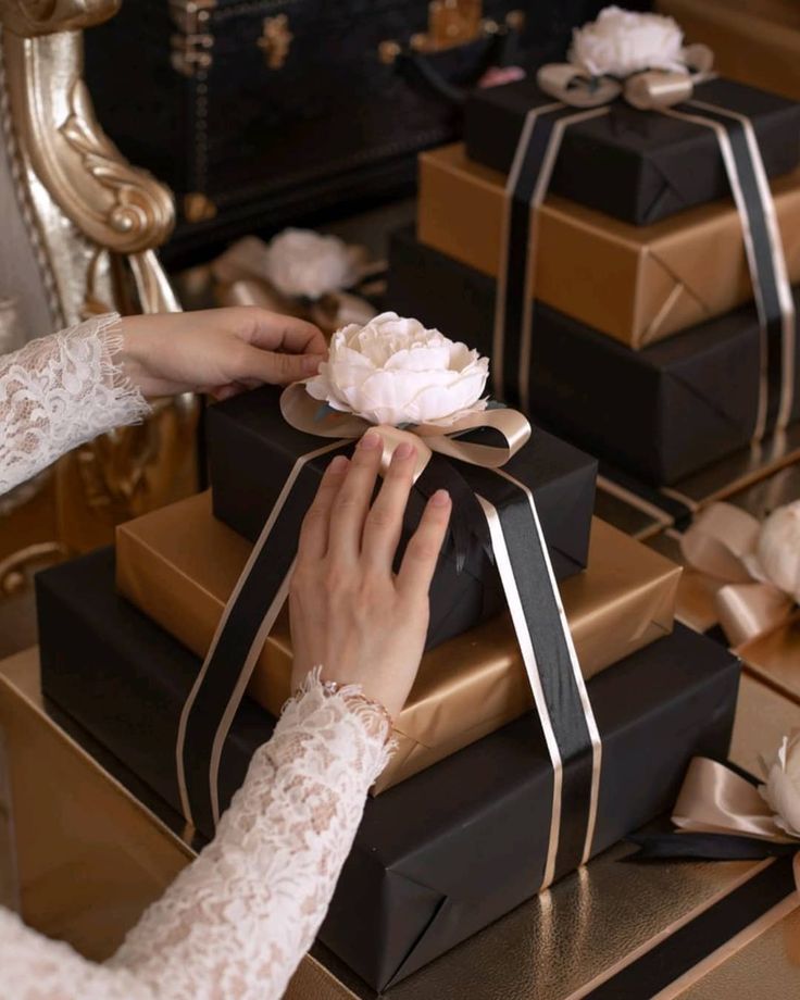 a woman is wrapping presents in black and gold boxes with white flowers on each one