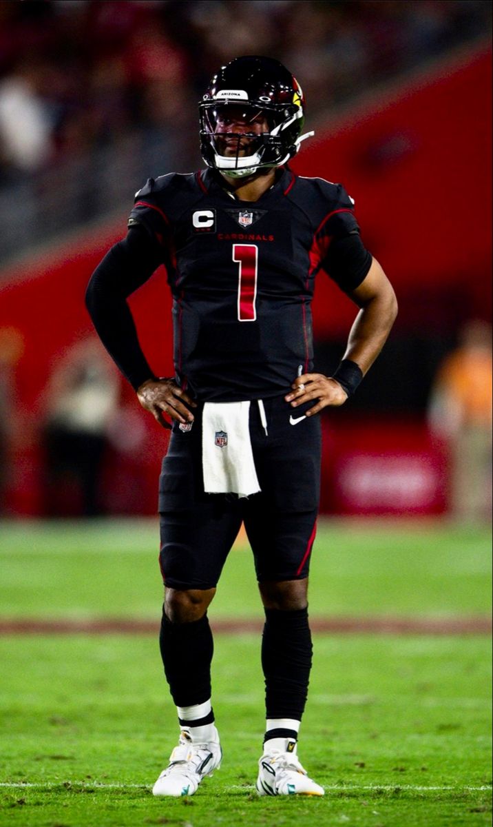 a football player is standing on the field with his hands on his hips while wearing a black uniform