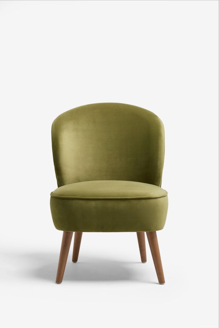 a green chair sitting on top of a white floor next to a wooden leg lamp