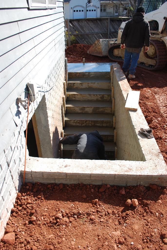 a man standing next to a building with stairs going up it's side in the dirt