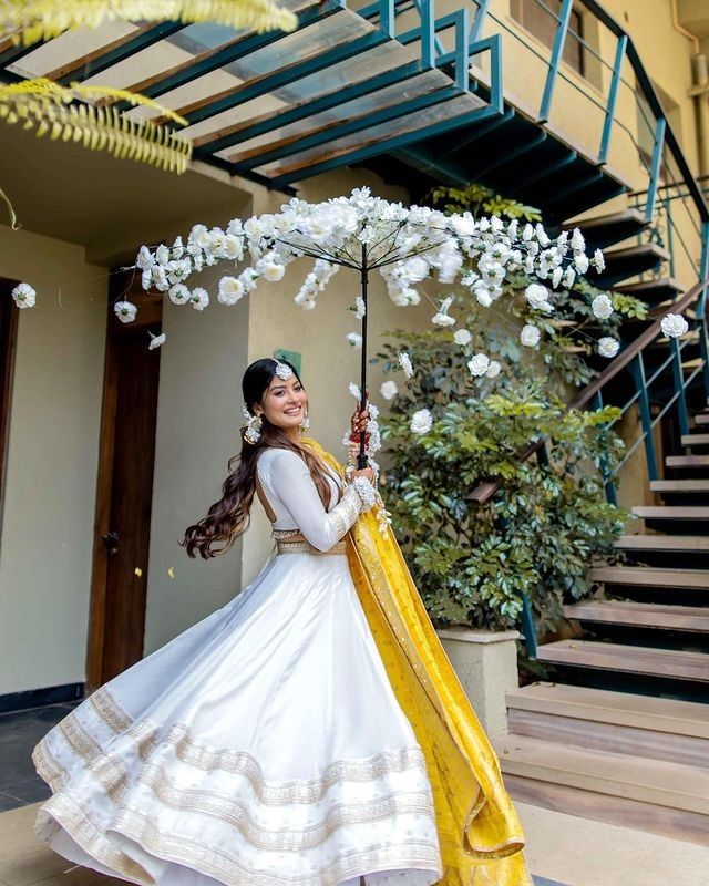 a woman in a white and yellow dress holding an umbrella with flowers on the ground