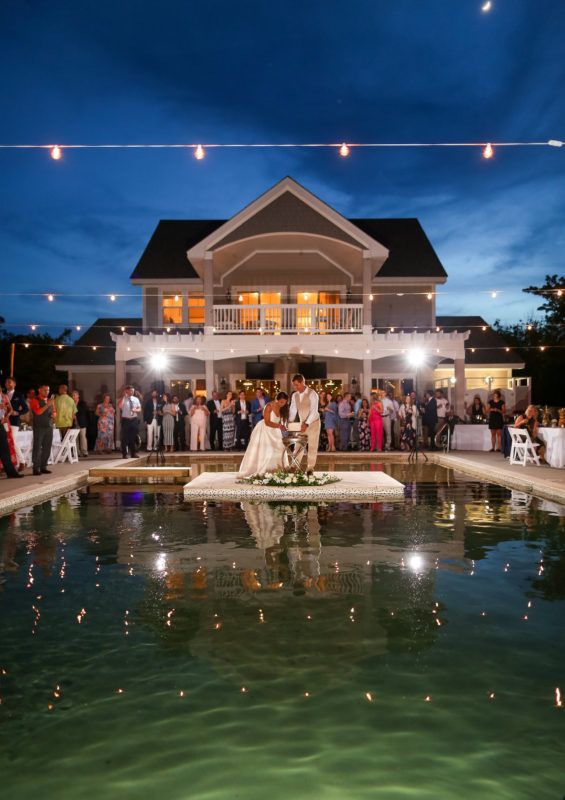 a bride and groom standing in front of a pool at night with their wedding party