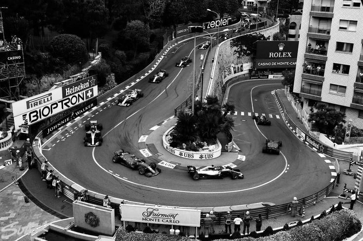 an aerial view of a race track with cars driving on it and buildings in the background