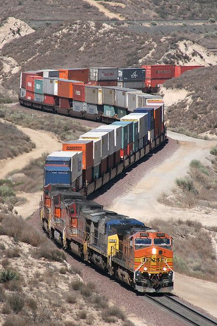 two trains are traveling down the tracks in an open area with hills and scrub brush