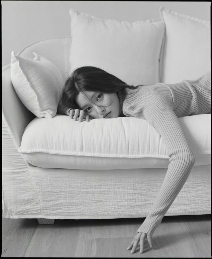 a woman laying on top of a white couch next to pillows and pillowcases