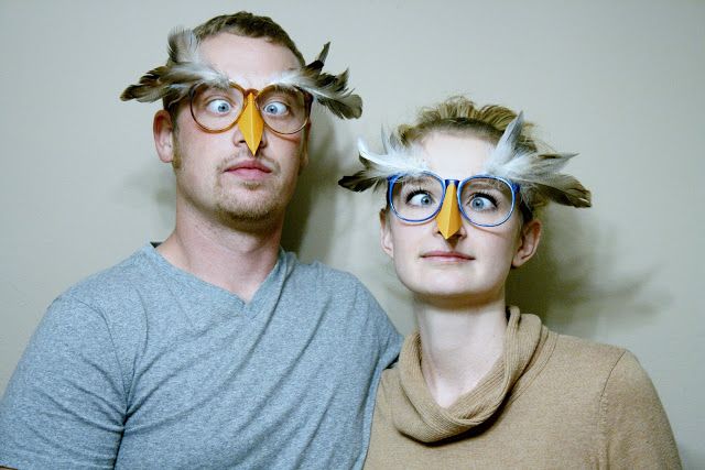 two people with fake birds on their heads posing for a photo in front of a wall