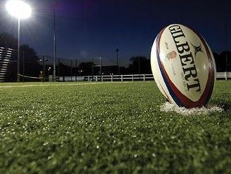 a rugby ball sitting on top of a lush green field under a stadium light at night