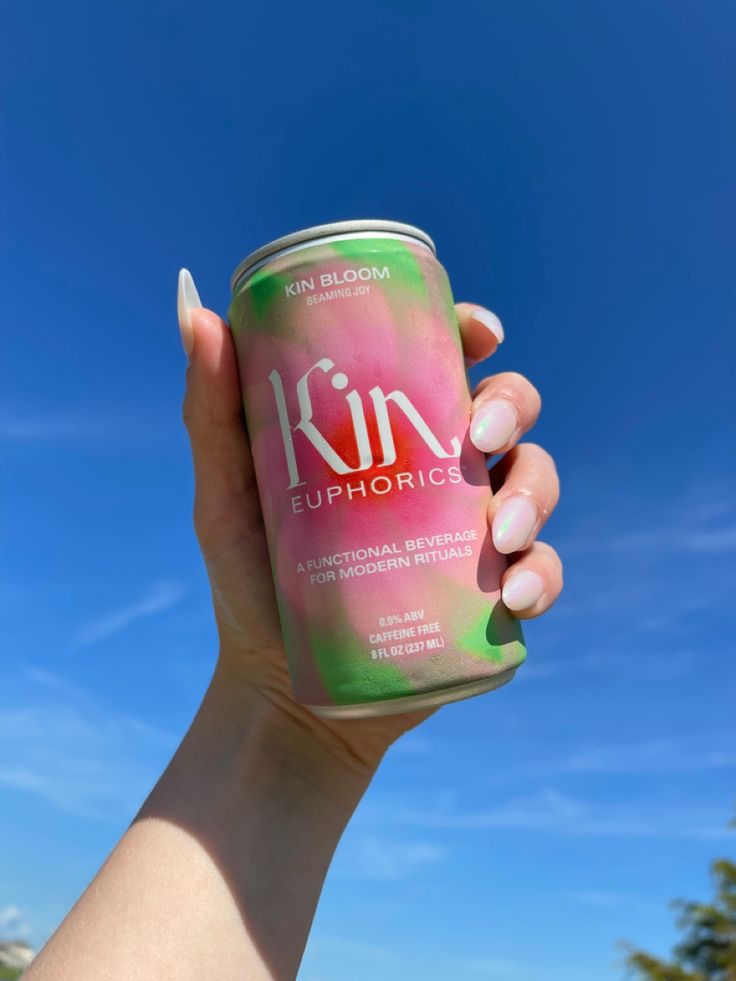 a person holding up a can of drink in front of a blue sky with clouds