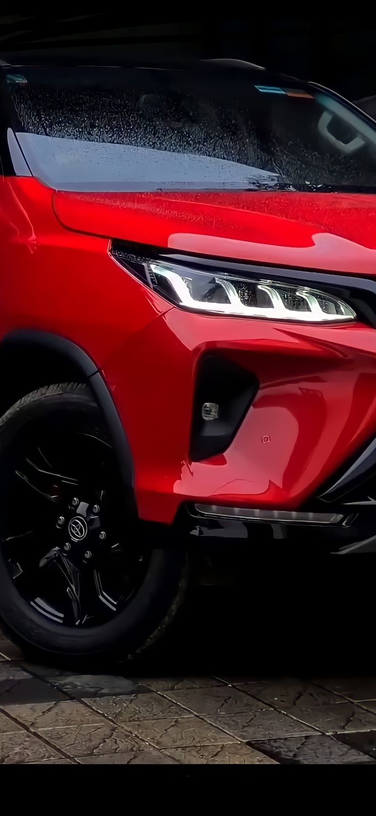 the front end of a red suv parked in a parking lot with its lights on