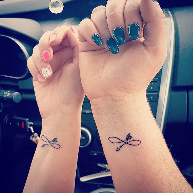 two people holding hands with tattoos on their wrists and wristbands, in front of the steering wheel of a car