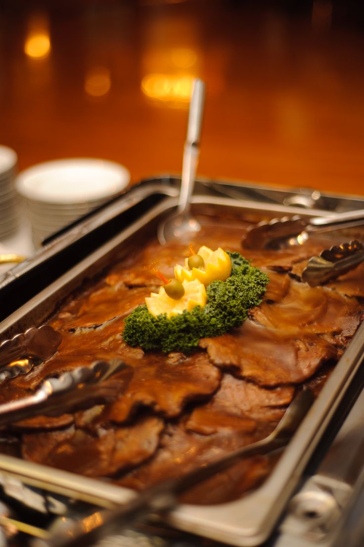 a tray filled with meat and broccoli on top of a wooden table next to silverware