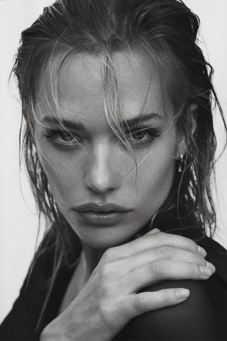 a black and white photo of a woman with her hand on her shoulder looking at the camera