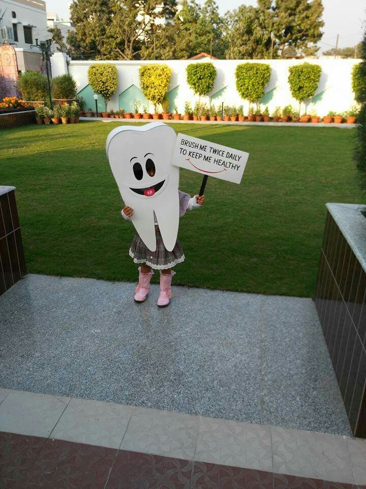 a person holding a sign with a tooth on it in front of some grass and bushes