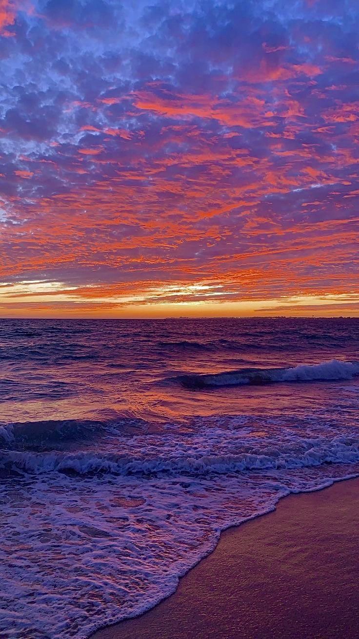 the sun is setting over the ocean with waves coming in