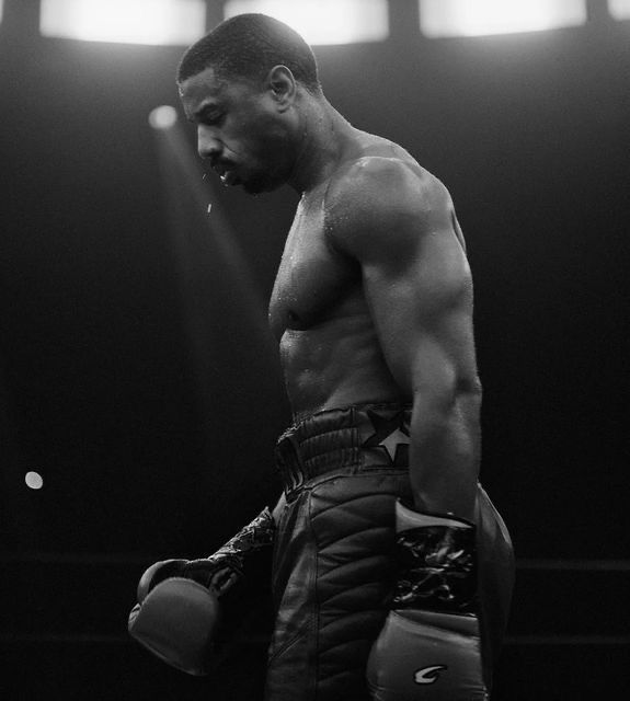 a black and white photo of a man with boxing gloves on his chest, standing in the middle of a ring