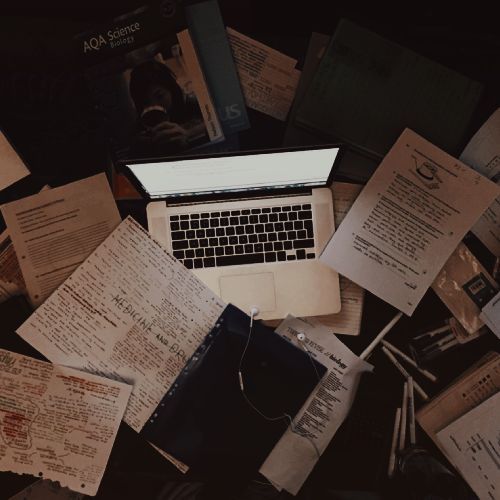 an open laptop computer sitting on top of a pile of papers next to each other