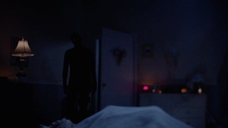 a person standing in a dark room next to a bed