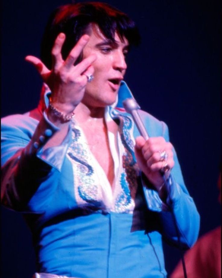 a woman holding a microphone up to her face while wearing a blue shirt and silver pants