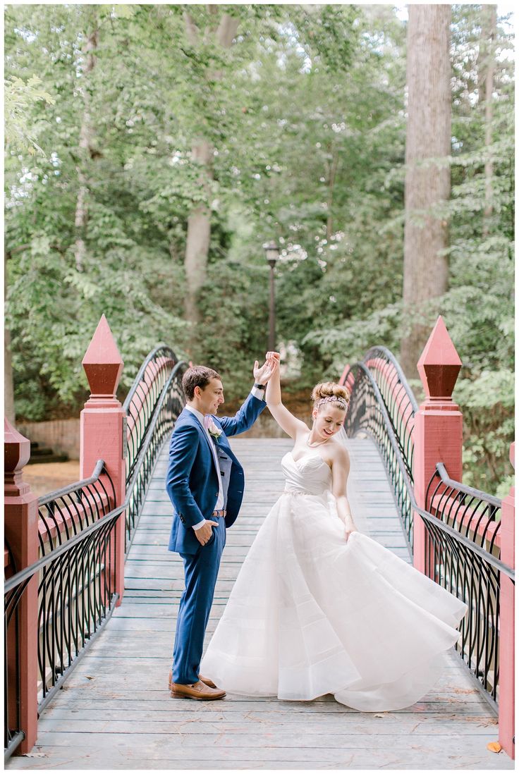 a bride and groom standing on a bridge in the woods holding each other's hands