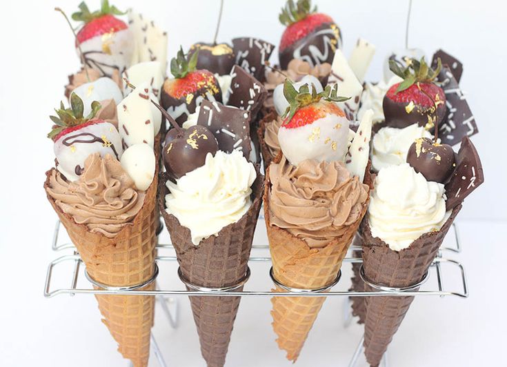 chocolate covered ice cream cones with strawberries in them on a wire rack against a white background