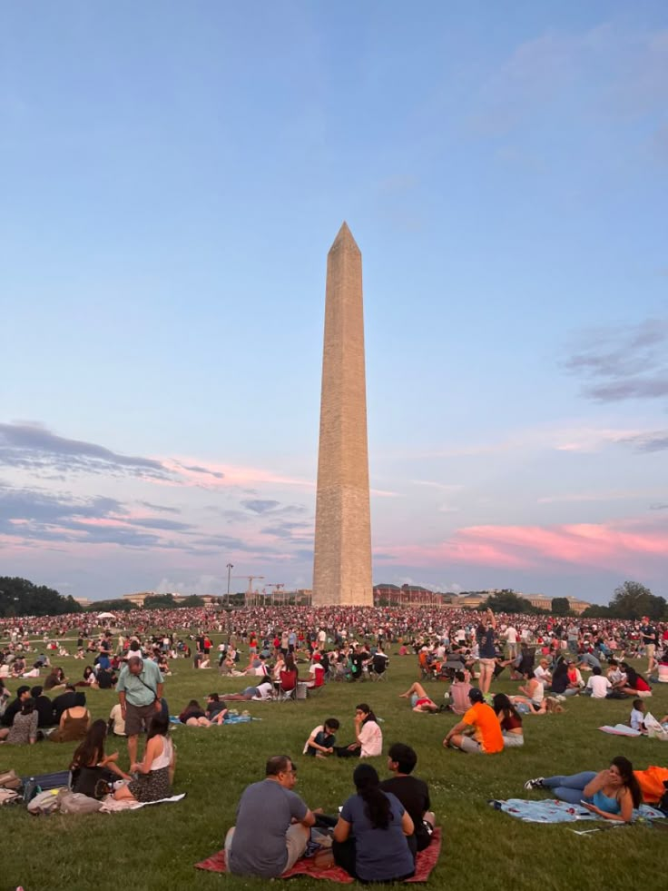 many people are sitting on the grass in front of the washington monument at sunset or dawn