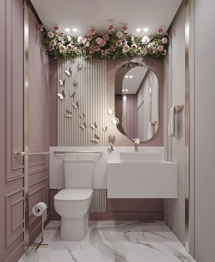 a white toilet sitting next to a sink in a bathroom under a mirror and flowers on the wall