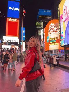 a woman is standing in the middle of a busy city street at night with billboards on both sides