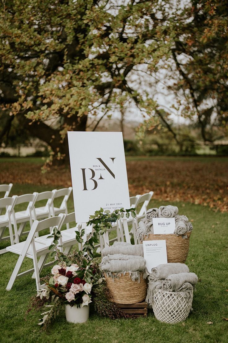 an outdoor ceremony setup with white chairs and baskets filled with flowers, greenery and blankets