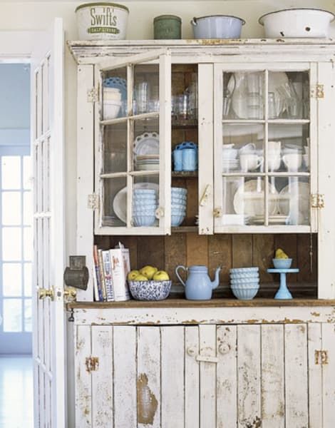 an old china cabinet with glass doors and dishes on it's top, in a kitchen