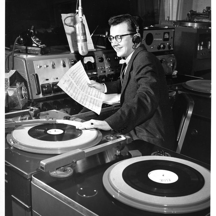 a man sitting at a record player with headphones on and reading a paper in front of him