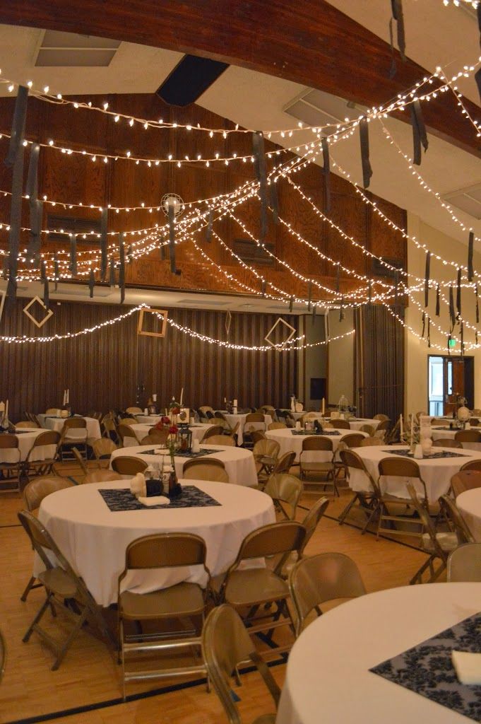 a banquet hall with tables and chairs covered in white tablecloths, lights strung from the ceiling