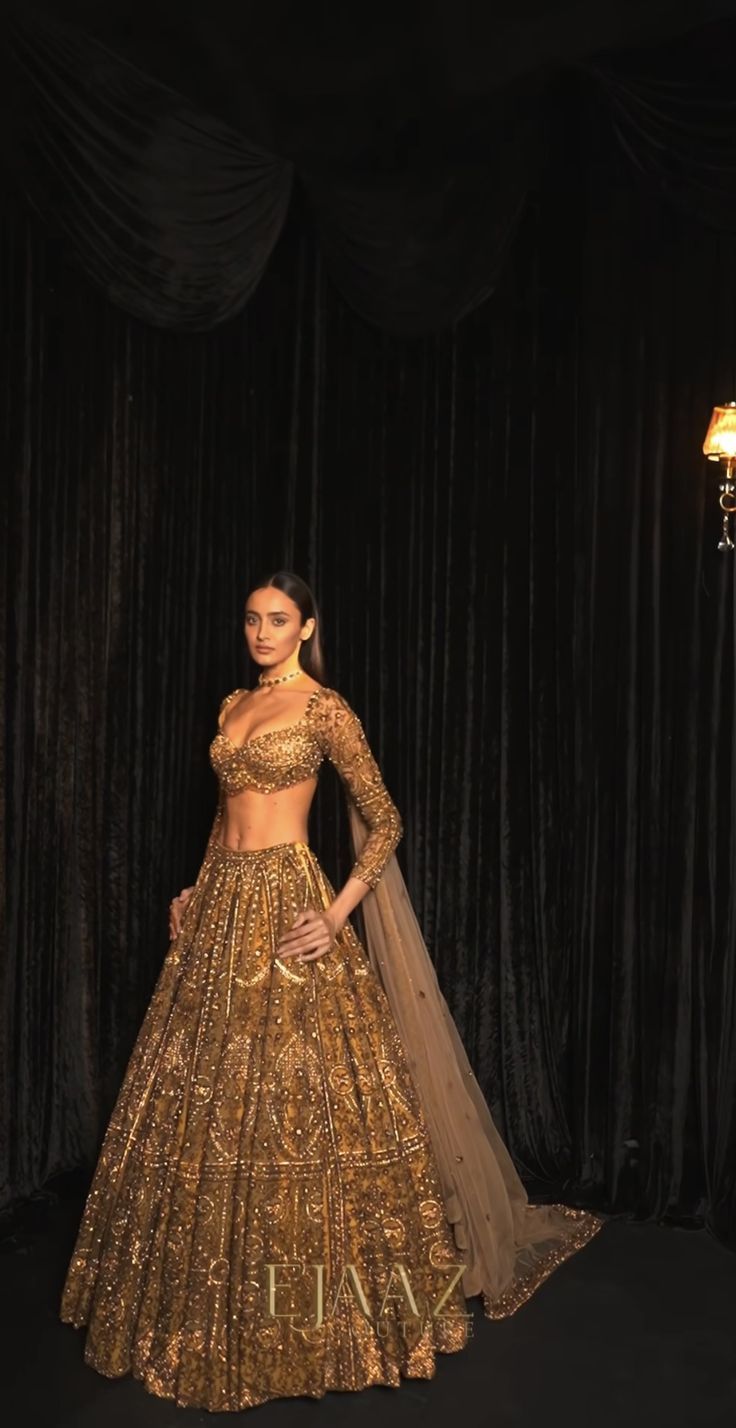 a woman in a gold lehenga standing next to a black curtain with lights on it