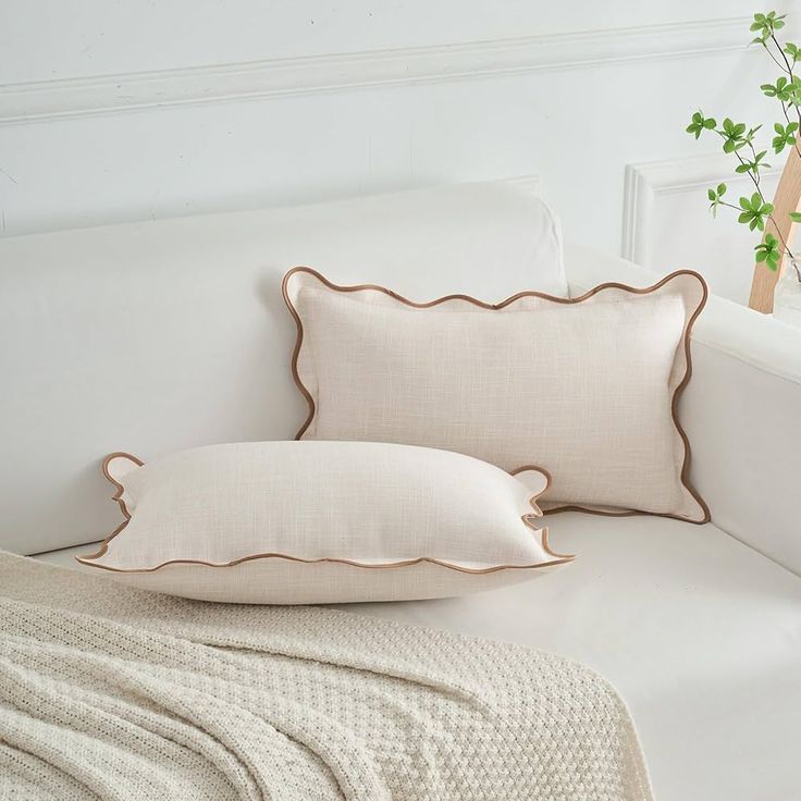 two pillows sitting on top of a white couch next to a potted green plant