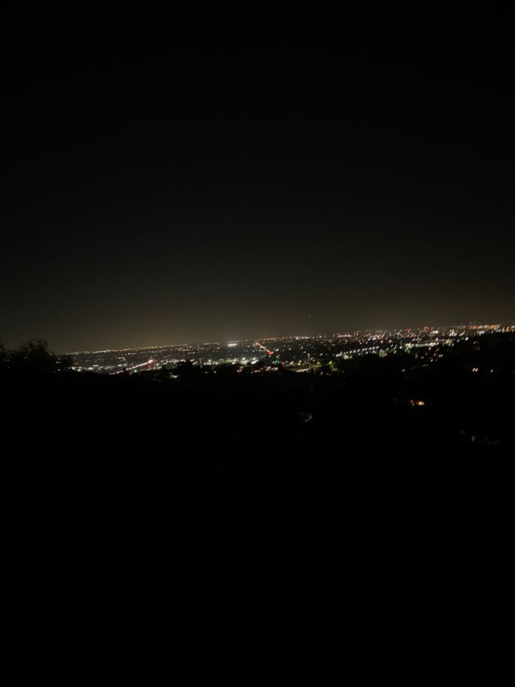 the city lights are lit up in the dark night sky over trees and hills below