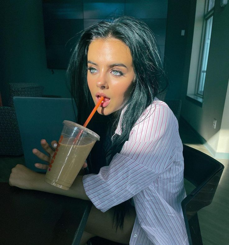 a woman sitting at a table with a drink in her hand and a straw in her mouth